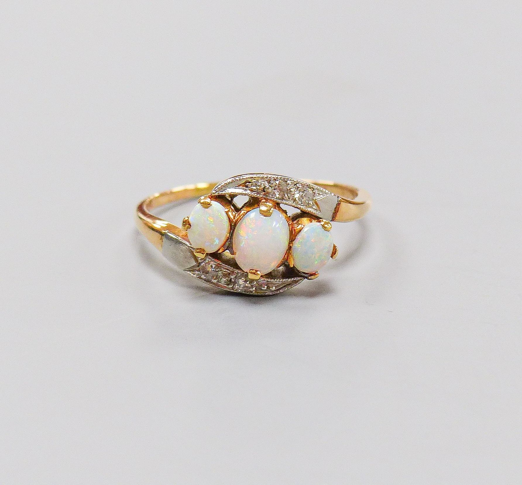 An 18ct and plat, three stone white opal and diamond chip set crossover ring, size S, gross weight 4.1 grams.